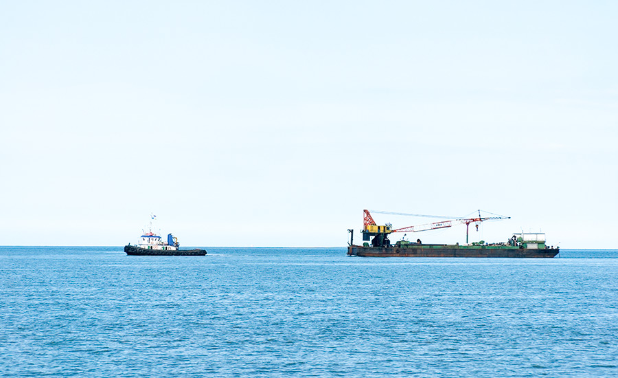 Two ships equipped for cross-border transportation using precise trajectory positioning systems, cruising on open sea under a clear sky.